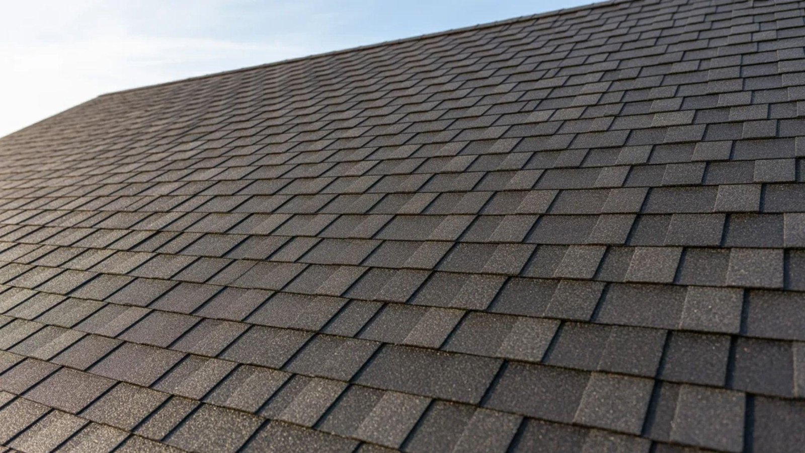 A close-up view of a house roof featuring traditional asphalt shingles in a neat, overlapping pattern.