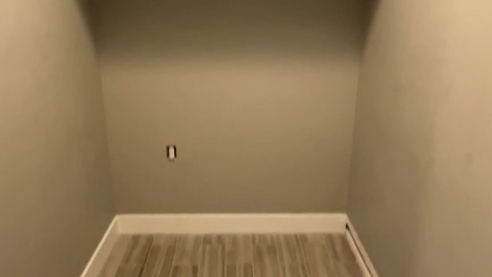 A corridor with a light switch mounted on the wall beside a door, leading to another room.