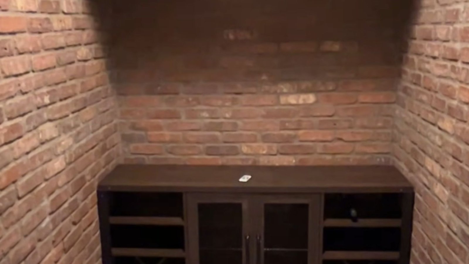 A brick wall with a flat-screen TV and a stylish cabinet below it.r