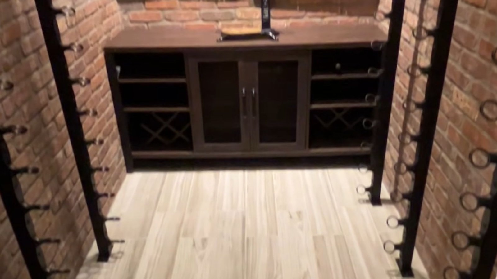 Interior of a wine cellar with a brick wall and neatly arranged shelves displaying an assortment of wine bottles.