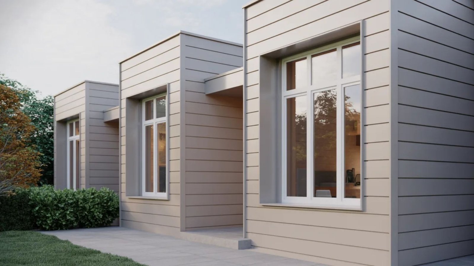 Modern, minimalist building with horizontal beige panels and large windows reflecting trees and sky. Green shrubs and grass border a concrete walkway.
